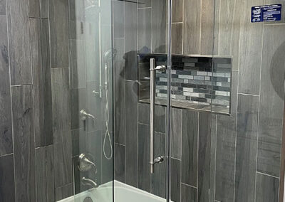 “Modern frameless barn-door sliding shower enclosure featuring a buttress fixed panel and clear glass, installed by A Cut Above Glass in Scottsdale, Arizona.”